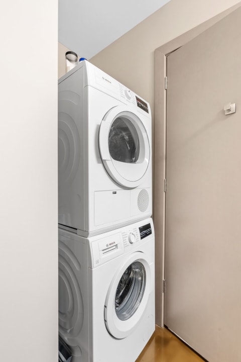 Stacked white washing machine and dryer in a small laundry area.