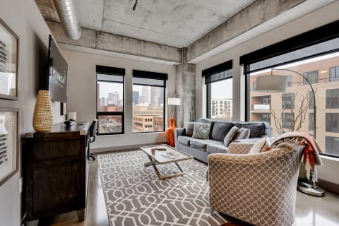 Modern living room with gray sofa, patterned armchair, and city skyline view through large windows.