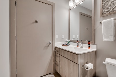 Modern bathroom featuring a beige door, white vanity, large mirror, and accessories.