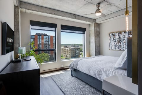 A stylish modern bedroom featuring a bed, large windows, and contemporary art.