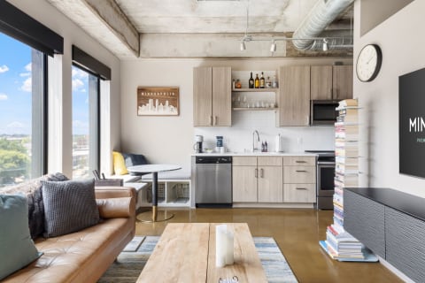 A stylish living room featuring a leather couch, dining table, modern kitchen, and large windows.