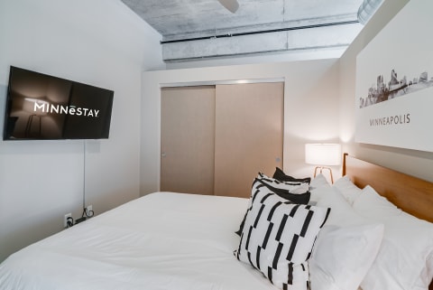 A cozy bedroom with a flat-screen TV, decorative pillows, and modern decor elements.