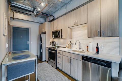 Modern kitchen with stainless steel appliances, light wood cabinets, and a small dining area.