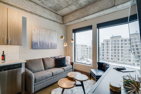 Modern living room with a gray sofa, wooden coffee tables, and large windows.