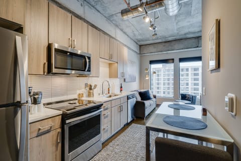 A modern kitchen with stainless steel appliances and a cozy living area featuring a gray sofa.