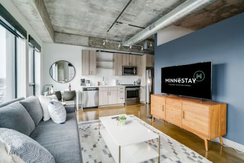 Modern living room with a gray sofa, wooden accents, and a contemporary kitchen.