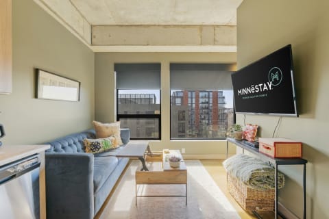 Modern living room with a blue sofa, wooden coffee table, and a TV displaying the MINNESTAY logo.