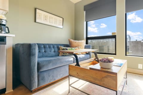 A living space with a blue velvet sofa, wooden coffee table, and bright windows.