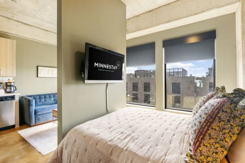 A stylish studio apartment with a comfy bed, television, sofa, and kitchenette.