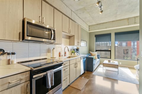 Contemporary kitchen and living area featuring a blue couch and large windows.