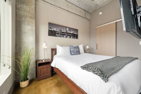 A contemporary bedroom with a large bed, wooden nightstand, and potted plant, adorned with a skyline photograph.