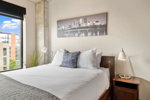 Cozy bedroom with a bed, city skyline art above, and a window view.