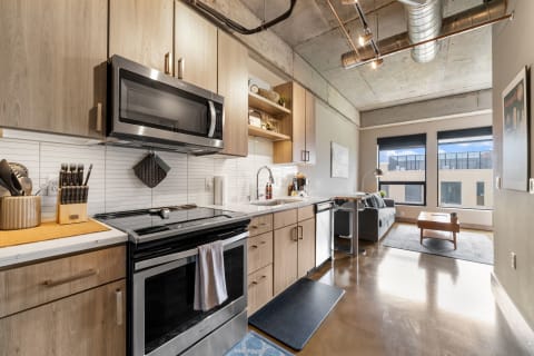 Modern kitchen with light wood cabinetry and stainless steel appliances, leading to a cozy living area with natural light.