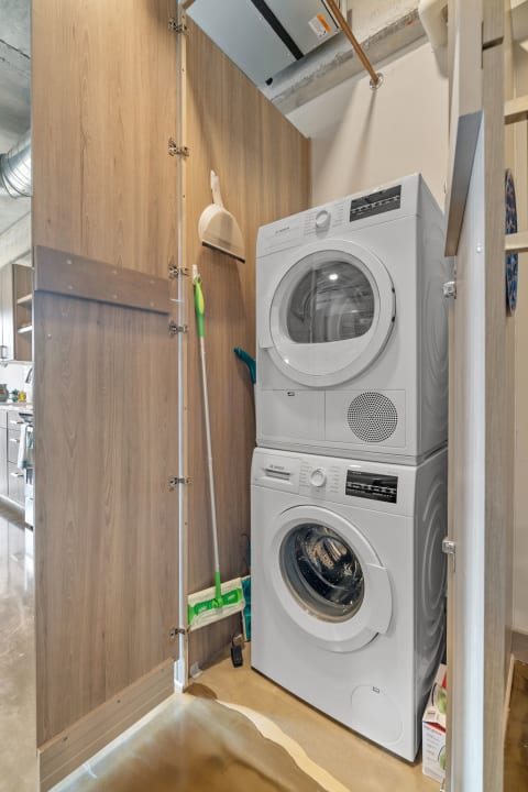 Compact laundry area featuring a stacked washer and dryer with cleaning tools nearby.