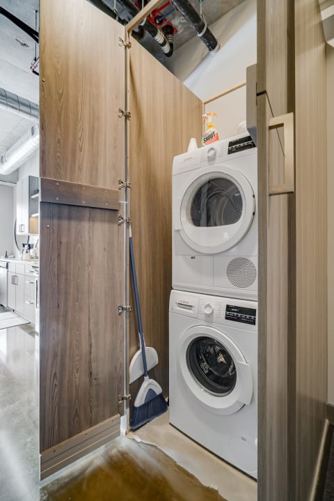 Stacked Bosch washer and dryer in a narrow laundry alcove next to a broom.