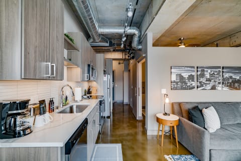 Modern apartment kitchen and living area with gray cabinets, white countertop, and industrial design.