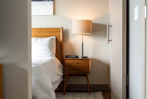 A bedroom featuring a wooden bed frame, nightstand, lamp, and soft bedding.