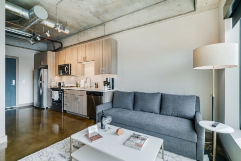 A contemporary apartment featuring a living area with a gray sofa and a kitchen with wooden cabinets.