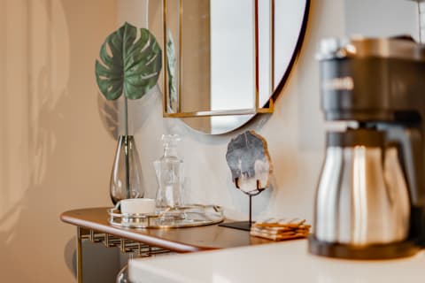 Modern tabletop featuring a glass vase with a green leaf, a decanter, coasters, a decorative stone, and a coffee maker.