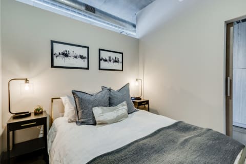 Stylish modern bedroom featuring a bed with decorative pillows, black nightstands, and city skyline artwork on the walls.