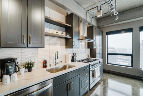 A contemporary kitchen with dark cabinets, stainless steel appliances, and large windows.