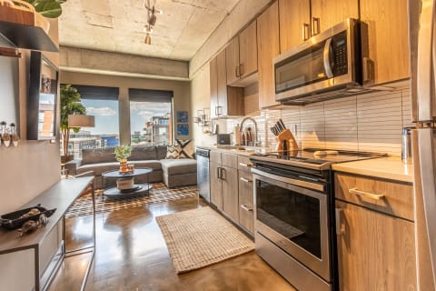 A beautifully designed kitchen and living area in an urban apartment, featuring wooden cabinets, stainless steel appliances, and a cozy couch.