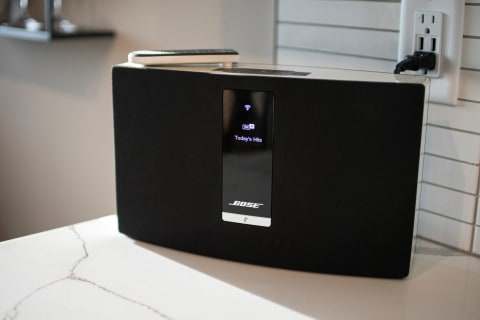 A black Bose speaker on a marble surface showing music streaming information.