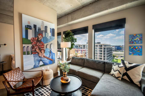 Living room with a large colorful painting, gray couch, and urban skyline view