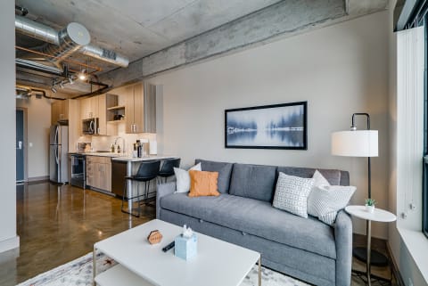 Modern apartment living room with gray sofa, coffee table, and kitchen in the background.