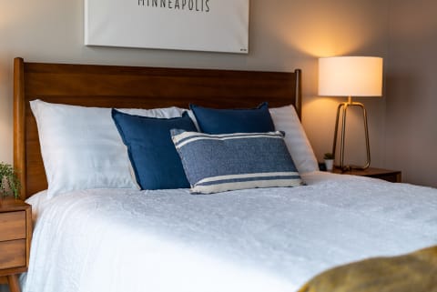 A neatly made bed with dark blue pillows and a decorative accent pillow in a modern bedroom setting.