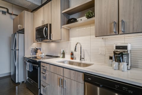 Modern kitchen with light wood cabinetry, stainless steel appliances, and a marble countertop.