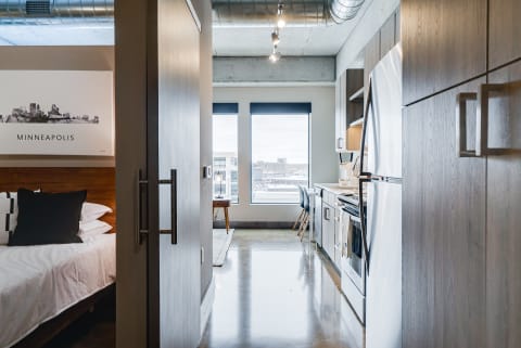 Interior view of a stylish studio apartment showcasing a bedroom and kitchen with large windows.