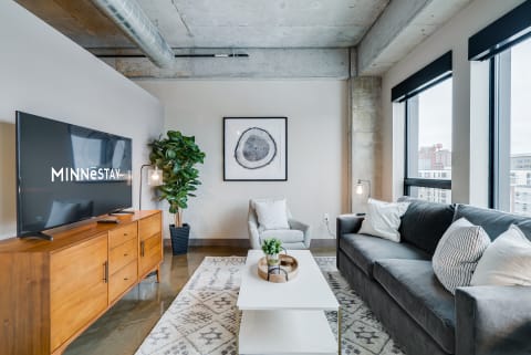 Modern living room featuring a gray sofa, wooden TV stand, and large windows with city view.