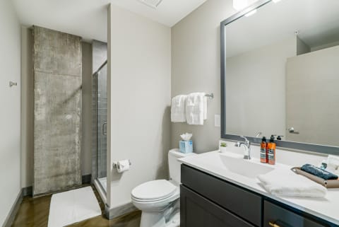 Modern bathroom with concrete wall, glass shower, and dark wooden vanity.