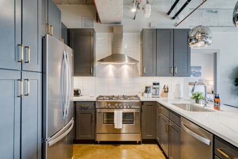 Modern kitchen featuring dark cabinets, stainless steel appliances, and marble countertops.
