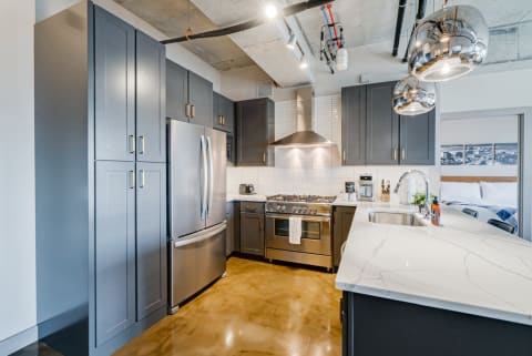 Modern kitchen with dark cabinets, stainless steel appliances, and a marble countertop.