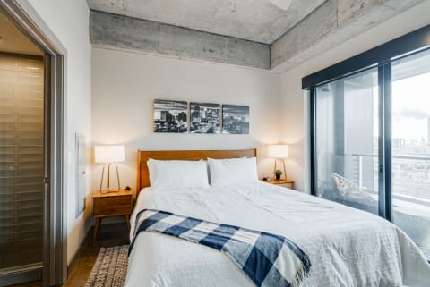 Contemporary bedroom interior with a bed, nightstand, and city views.