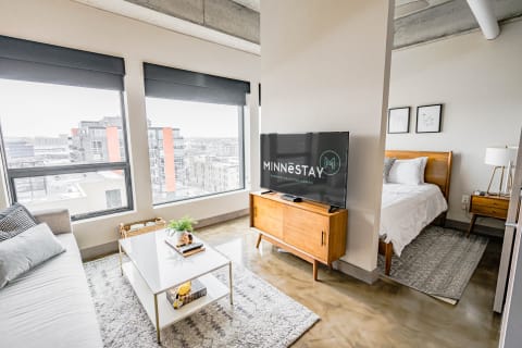 Stylish studio apartment with a gray couch, coffee table, and a large TV in front of city views.