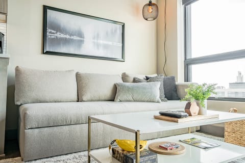 A light gray sectional sofa with cushions, a white coffee table, and a hanging light in a bright living space.