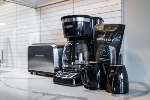 Black coffee maker, MINNESTAY coffee bag, and black coffee mugs on a kitchen counter.