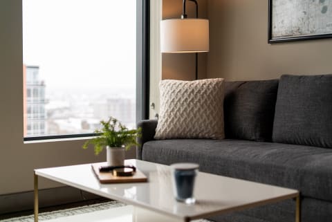A modern living room with a dark gray sofa, decorative pillow, white coffee table, and a window showing snowy cityscape.