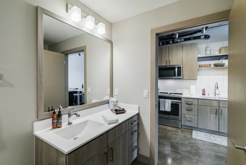 A contemporary bathroom with a large mirror and an adjoining kitchen area.
