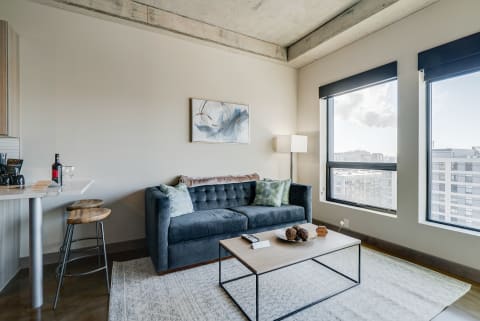 A chic modern living room featuring a sofa, coffee table, and large windows with city views.