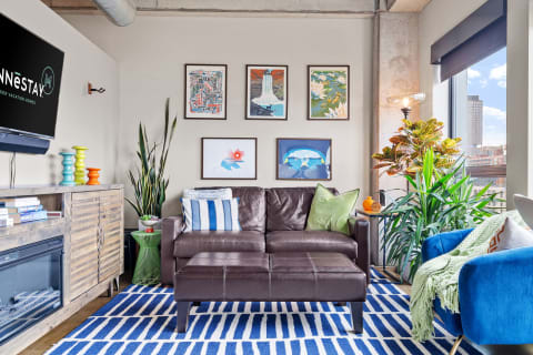 Modern living room featuring a brown leather sofa, colorful artwork, and indoor plants.
