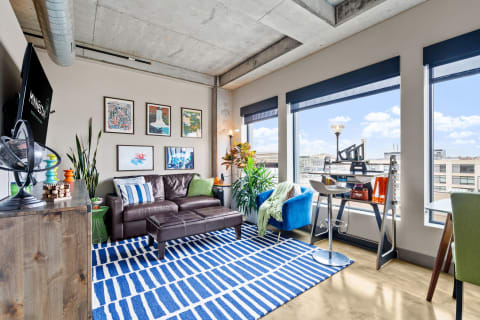 Stylish urban apartment living room with a leather sofa, colorful decor, and large windows.