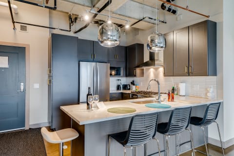 Modern kitchen with dark cabinets, a marble countertop, and pendant lighting.