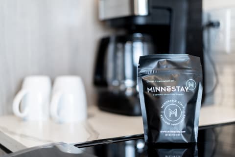 A coffee bag from MINNéSTAY in a modern kitchen beside white mugs and a coffee maker.