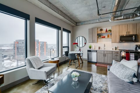 Interior of a modern apartment with large windows, a cozy living area, and a well-equipped kitchen.