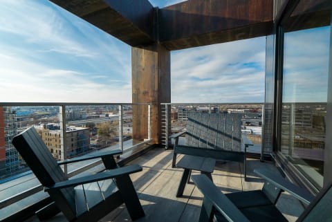 A high-rise balcony with Adirondack chairs looking over the city skyline on a clear day.