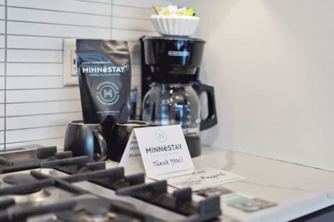 A stylish kitchen coffee station with black mugs, a coffee maker, and a thank you card from Minnestay.